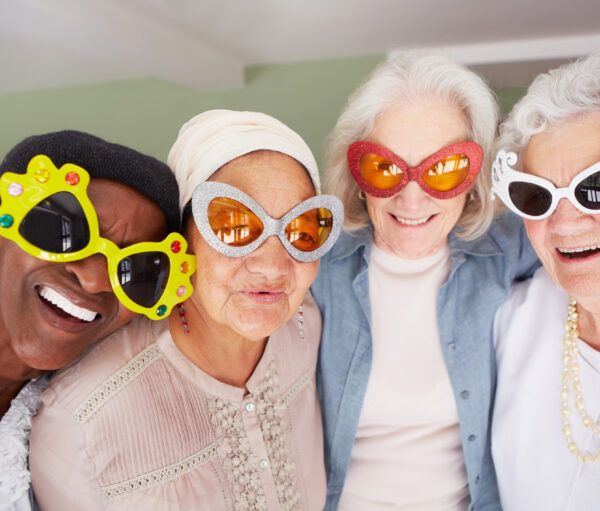 A group of elderly woman wearing funky sunglasses while standing in a nursing home
