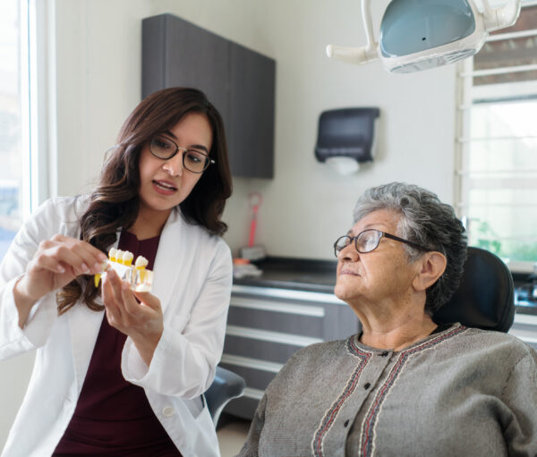 A latin female dentist and a senior patient looking at model teeth in the dental room.