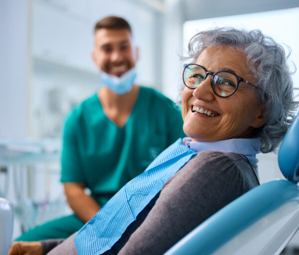 Happy senior woman at dental clinic looking at camera. Her dentist is in the background.