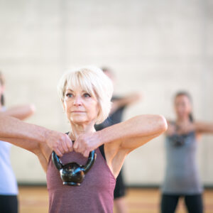 A fit senior Caucasian woman is carrying a dumbbell in her fitness class.
